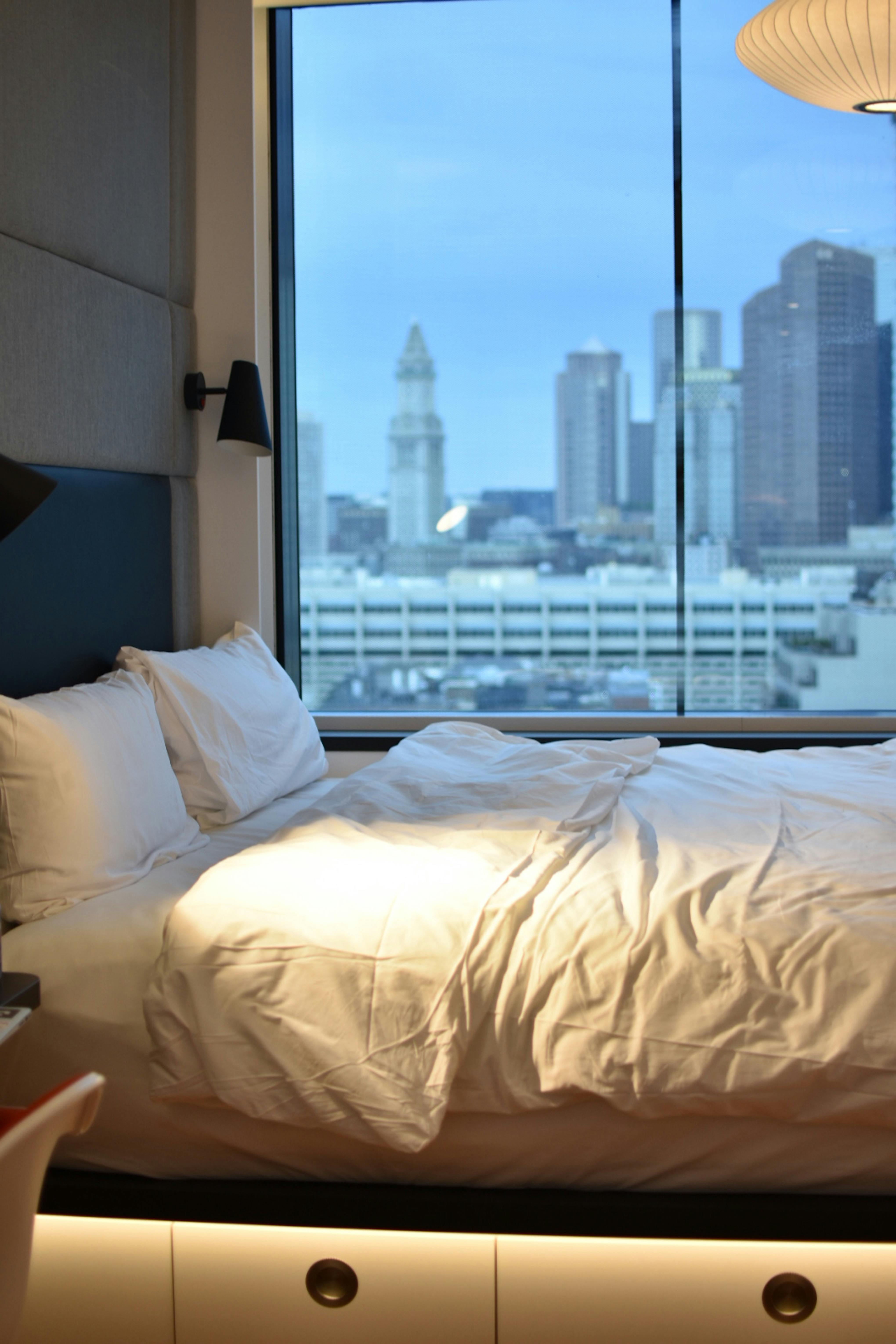 Bedin a bedroom with a window overlooking a city skyline