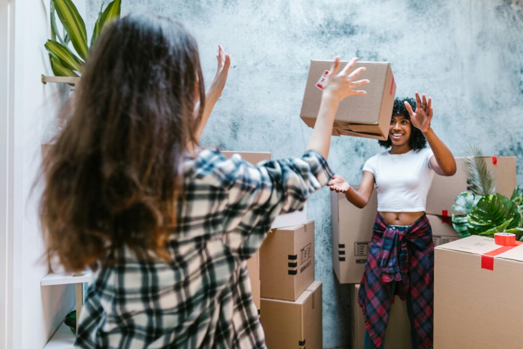 Two women joyfully unpacking boxes in their new home, showcasing friendship and a fresh start.